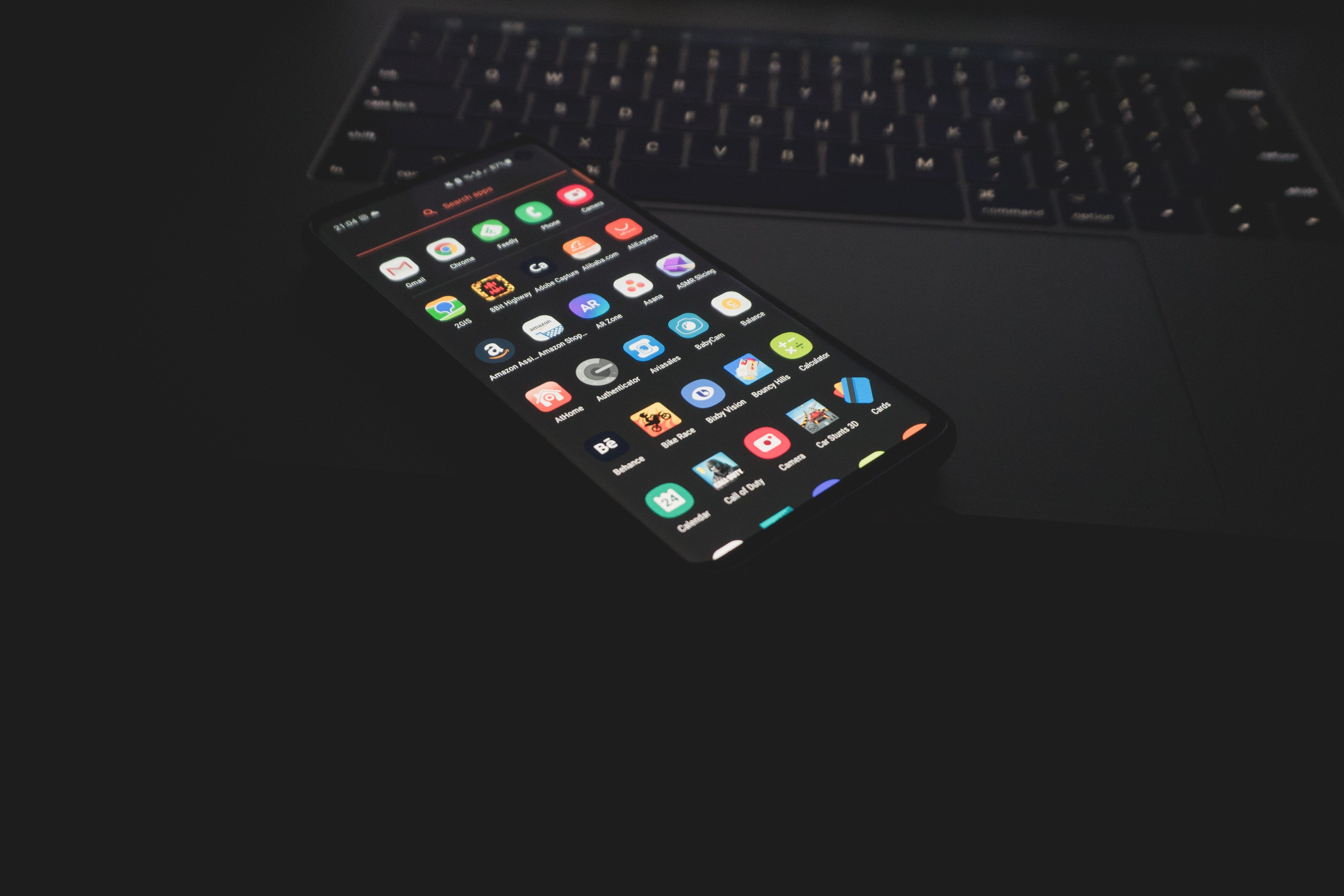 تُظهر الصورة هاتفًا يعمل بنظام التشغيل Android مفتوحًا مع ظهور أيقونات التطبيقات وهي موضوعة أعلى لوحة تتبع الكمبيوتر المحمول.