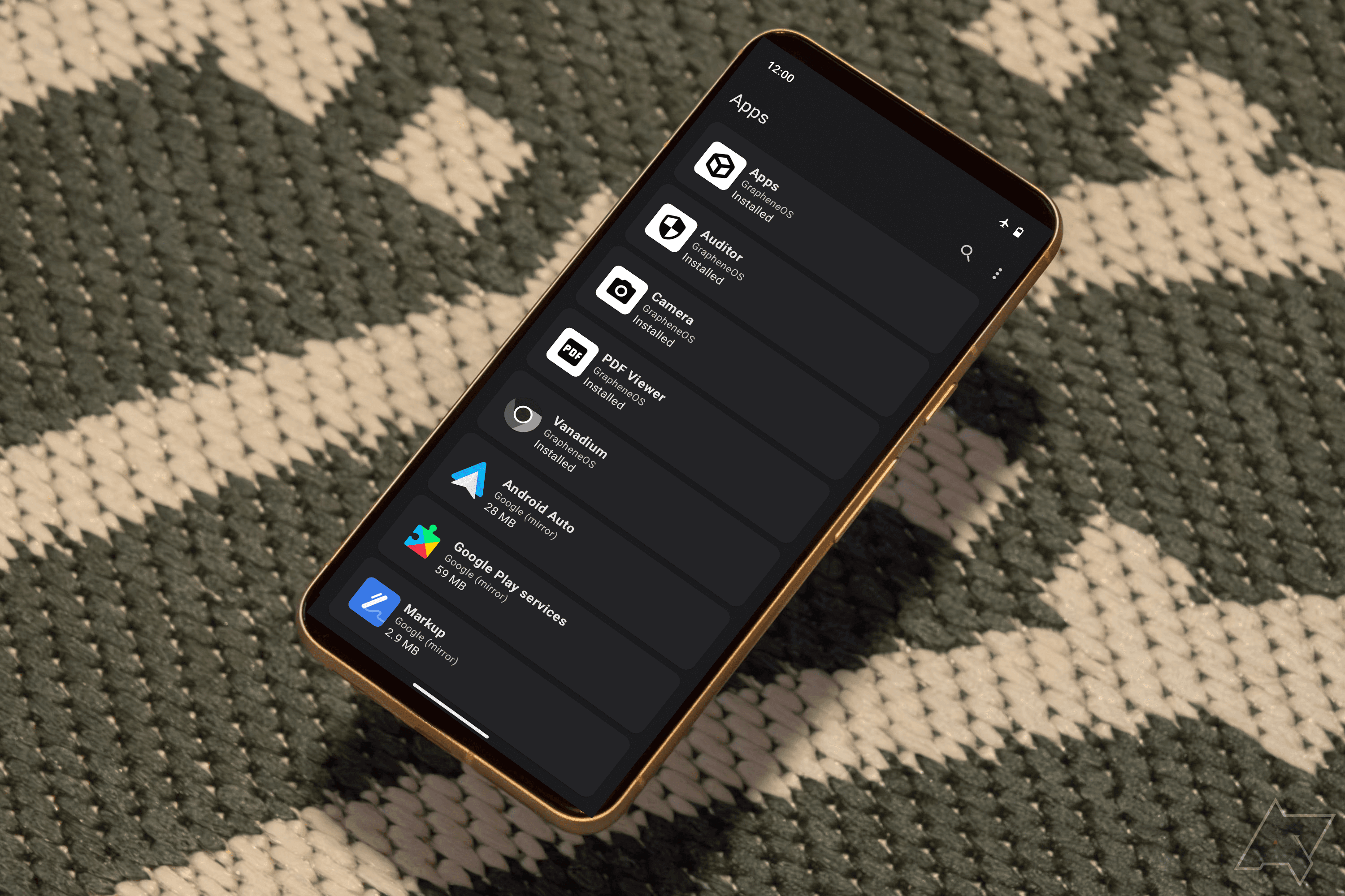 يوجد هاتف Pixel 8 مع قائمة إعدادات GrapheneOS فوق نسيج باللونين الأخضر والأبيض